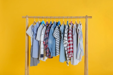 Rack with stylish children clothes on yellow background Photo of Rack with stylish children clothes on yellow background
