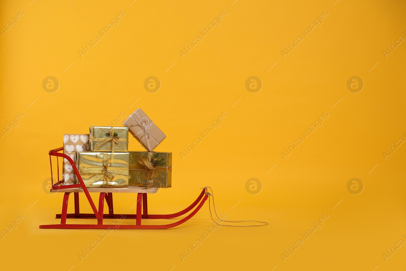 Sleigh with gift boxes on yellow background. Space for text Photo of Sleigh with gift boxes on yellow background. Space for text