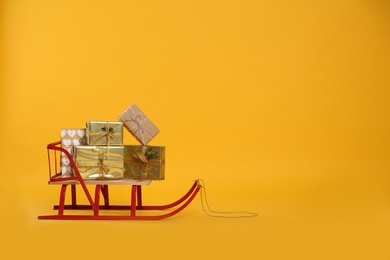 Sleigh with gift boxes on yellow background. Space for text Photo of Sleigh with gift boxes on yellow background. Space for text