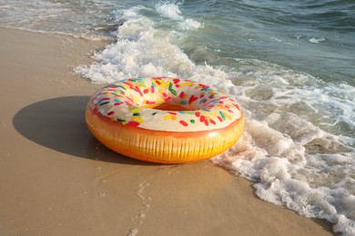 Inflatable ring with doughnut pattern on sandy beach near sea Photo of Inflatable ring with doughnut pattern on sandy beach near sea