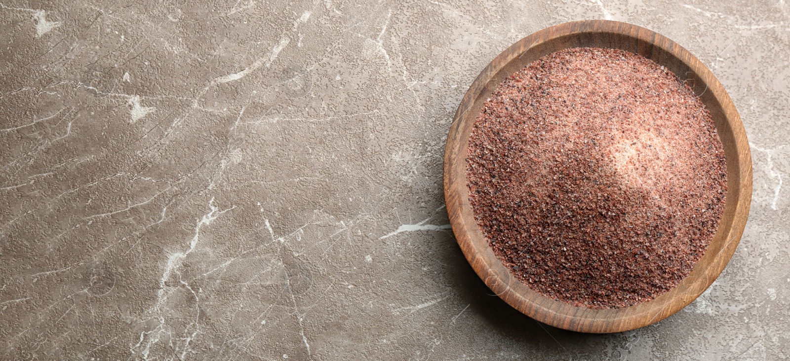 Photo of Ground black salt in wooden bowl on grey table, top view. Space for text