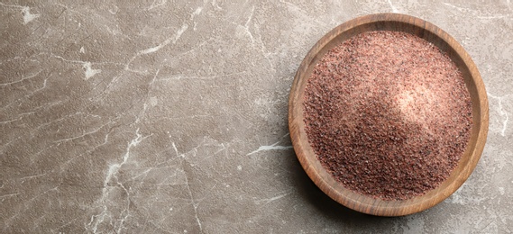 Ground black salt in wooden bowl on grey table, top view. Space for text Photo of Ground black salt in wooden bowl on grey table, top view. Space for text