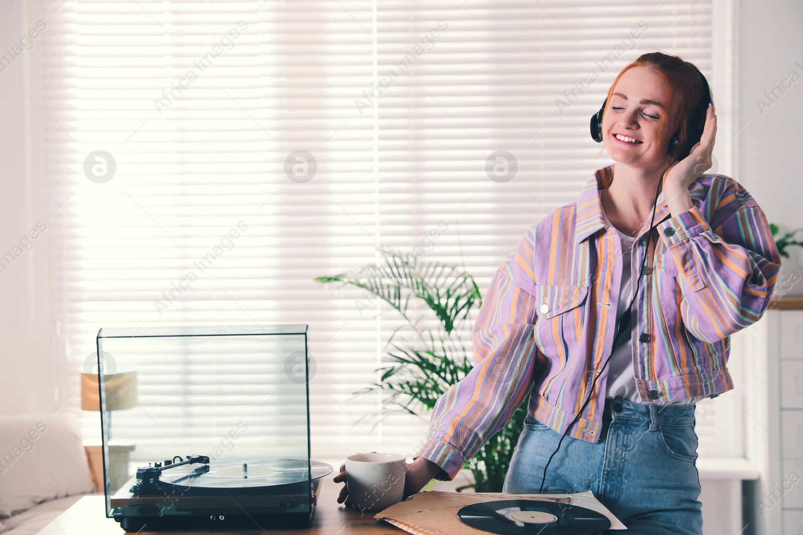 Young woman drinking coffee while listening to music with turntable at home Photo of Young woman drinking coffee while listening to music with turntable at home