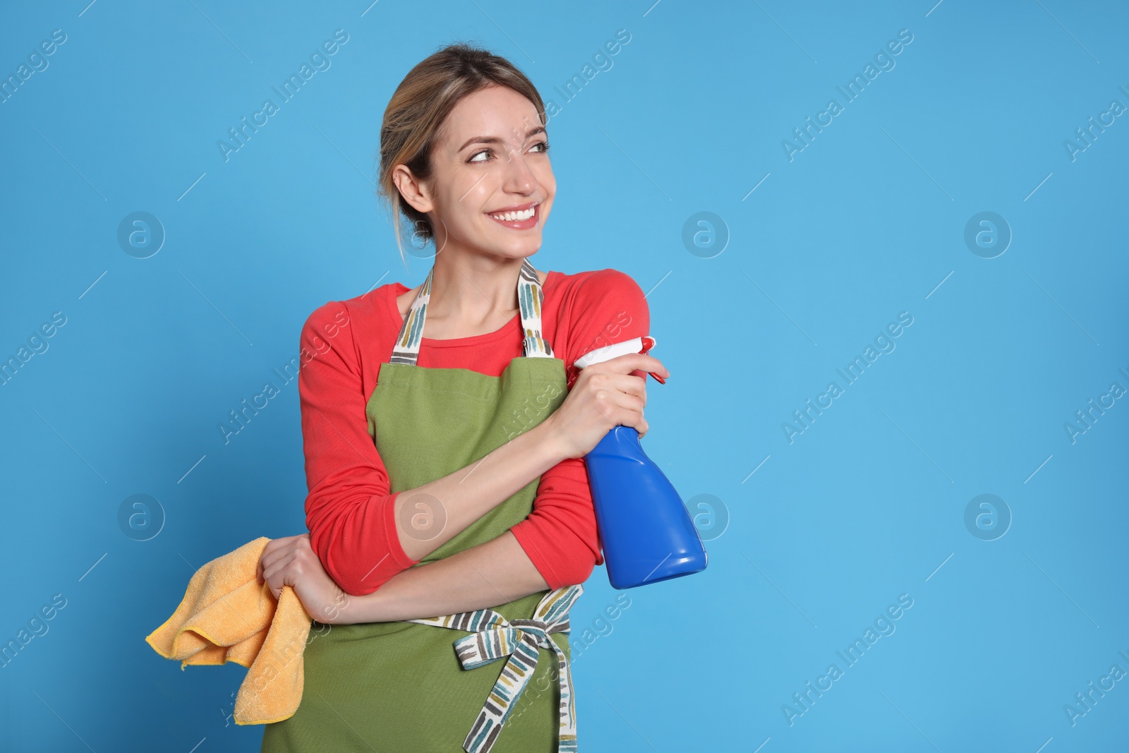 Young housewife with detergent and rag on light blue background. Space for text Photo of Young housewife with detergent and rag on light blue background. Space for text