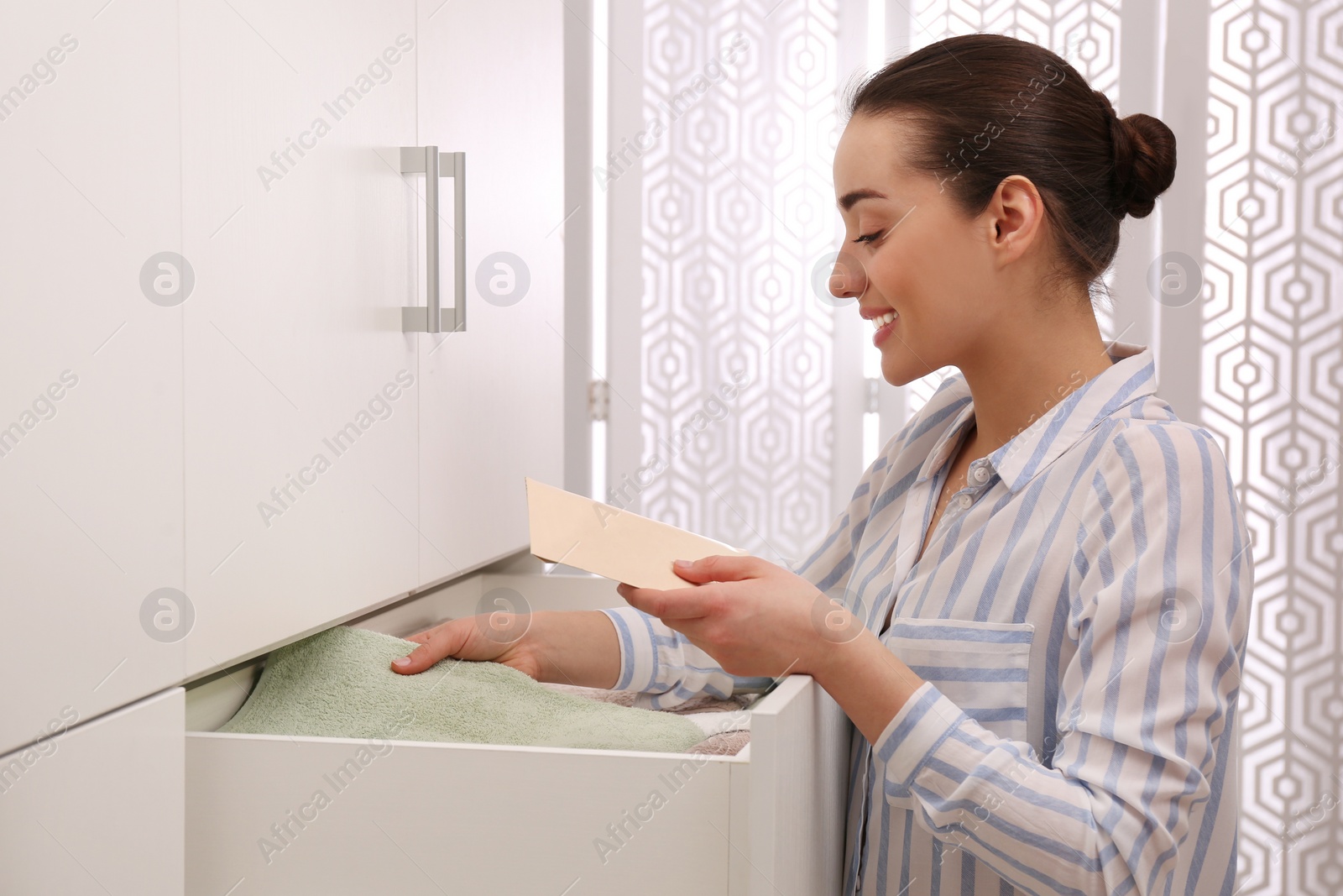 Woman putting scented sachet into drawer with towels indoors Photo of Woman putting scented sachet into drawer with towels indoors