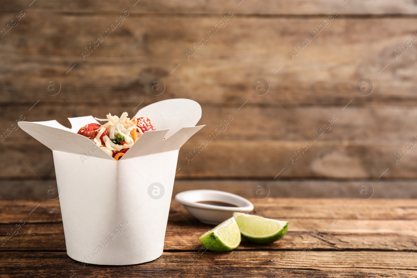 Photo of Box of vegetarian wok noodles with lime and soy sauce on wooden table. Space for text