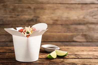 Photo of Box of vegetarian wok noodles with lime and soy sauce on wooden table. Space for text