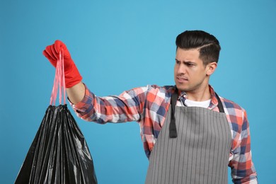Man holding full garbage bag on light blue background Photo of Man holding full garbage bag on light blue background