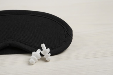 Photo of Pair of ear plugs and sleeping mask on white wooden background