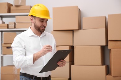 Young man with clipboard near cardboard boxes at warehouse Photo of Young man with clipboard near cardboard boxes at warehouse
