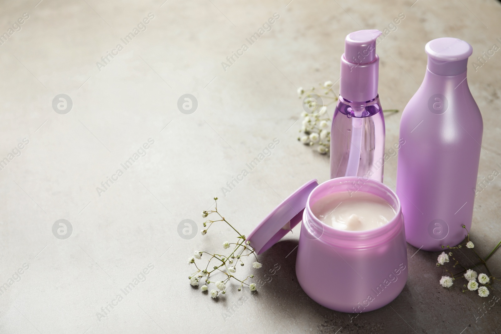 Set of hair cosmetic products and flowers on grey stone table. Space for text Photo of Set of hair cosmetic products and flowers on grey stone table. Space for text