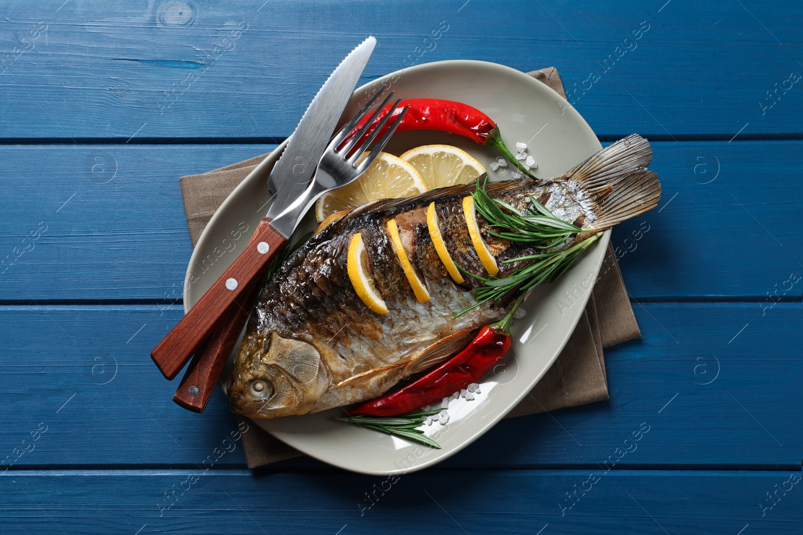 Photo of Tasty homemade roasted crucian carp served on blue wooden table, top view. River fish