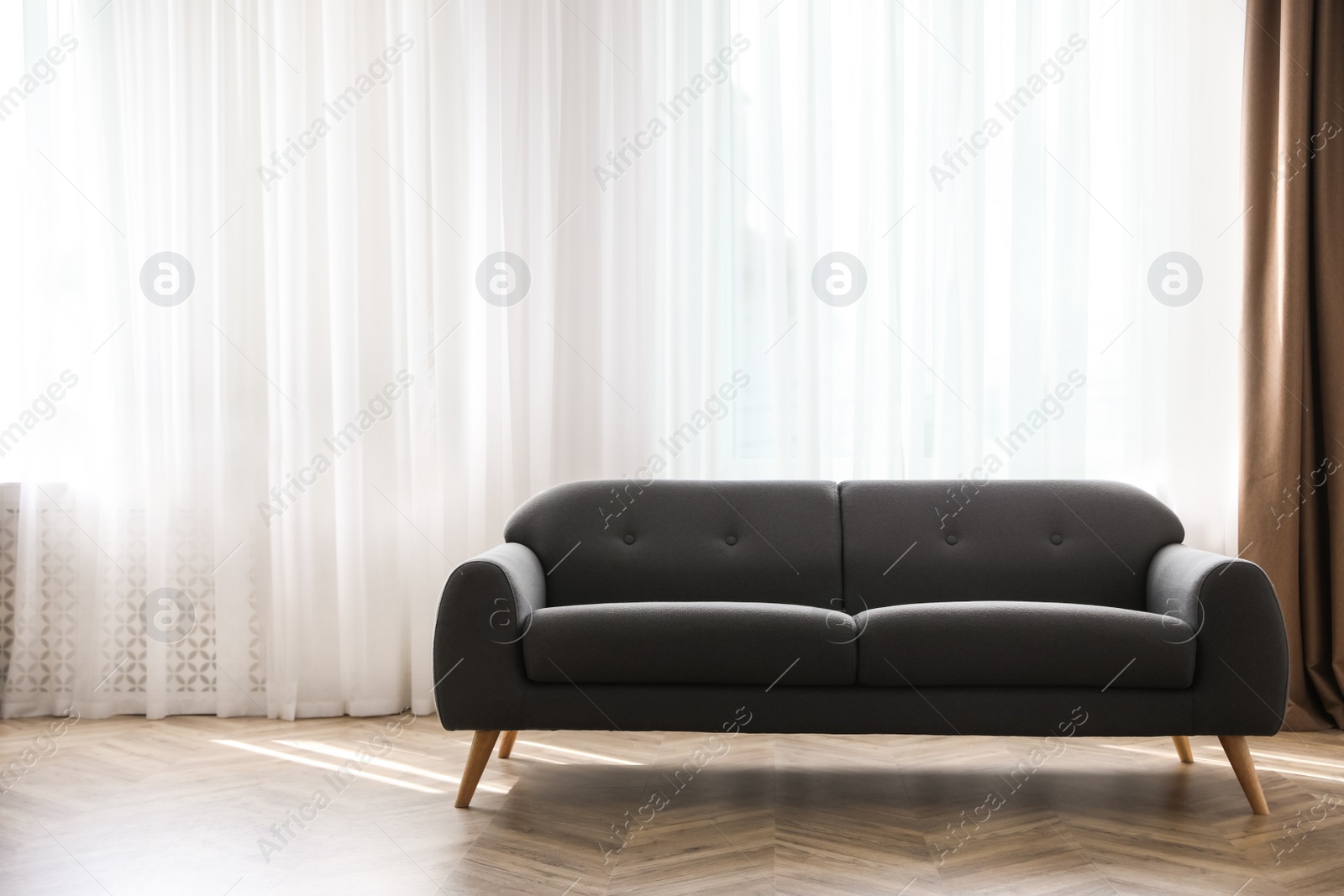 Comfortable grey sofa near window indoors, space for text. Interior design Photo of Comfortable grey sofa near window indoors, space for text. Interior design