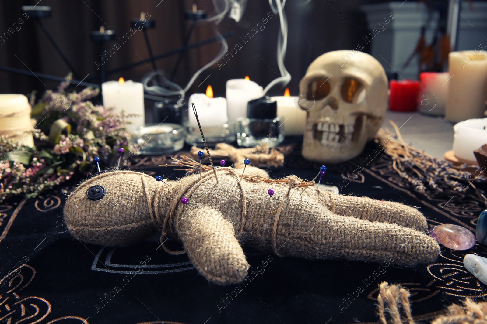 Voodoo doll with pins and dried flowers on table indoors Photo of Voodoo doll with pins and dried flowers on table indoors