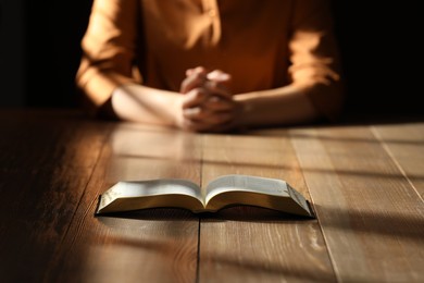 Religious woman praying over Bible at wooden table indoors, focus on book Photo of Religious woman praying over Bible at wooden table indoors, focus on book