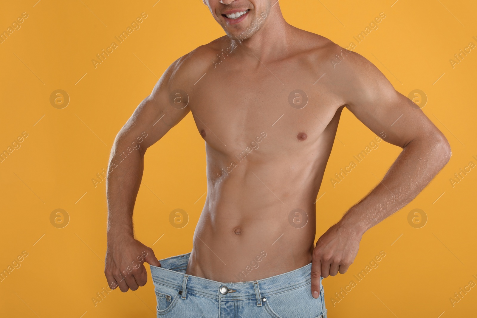 Photo of Shirtless man with slim body wearing big jeans on yellow background, closeup