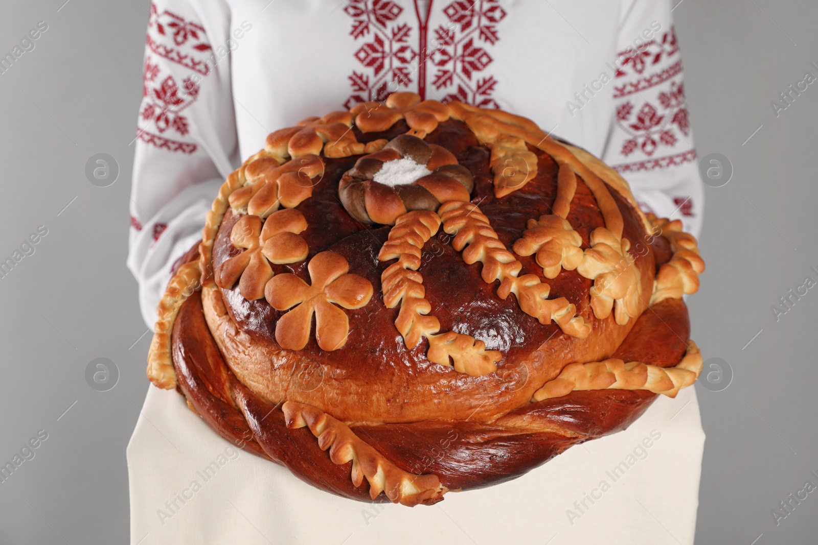 Woman with korovai on grey background, closeup. Ukrainian bread and salt welcoming tradition Photo of Woman with korovai on grey background, closeup. Ukrainian bread and salt welcoming tradition