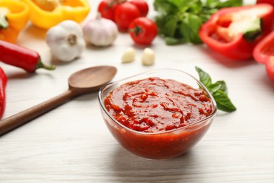 Delicious adjika sauce in glass bowl and ingredients on wooden table Photo of Delicious adjika sauce in glass bowl and ingredients on wooden table