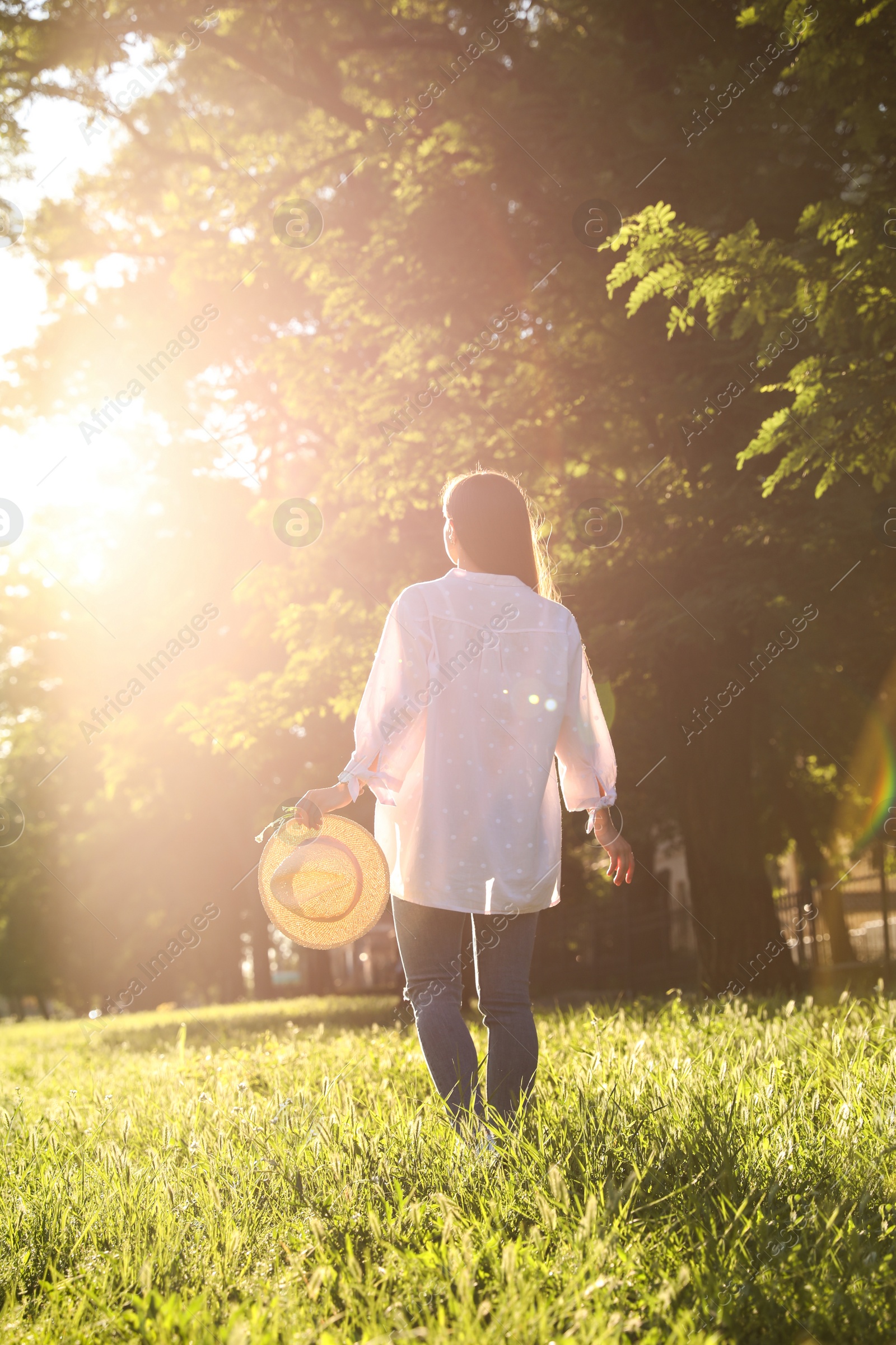 Young woman with straw hat outdoors on sunny day, back view Photo of Young woman with straw hat outdoors on sunny day, back view