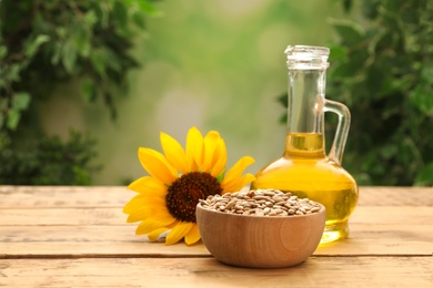 Sunflower, jug of oil and seeds on wooden table against blurred background Photo of Sunflower, jug of oil and seeds on wooden table against blurred background
