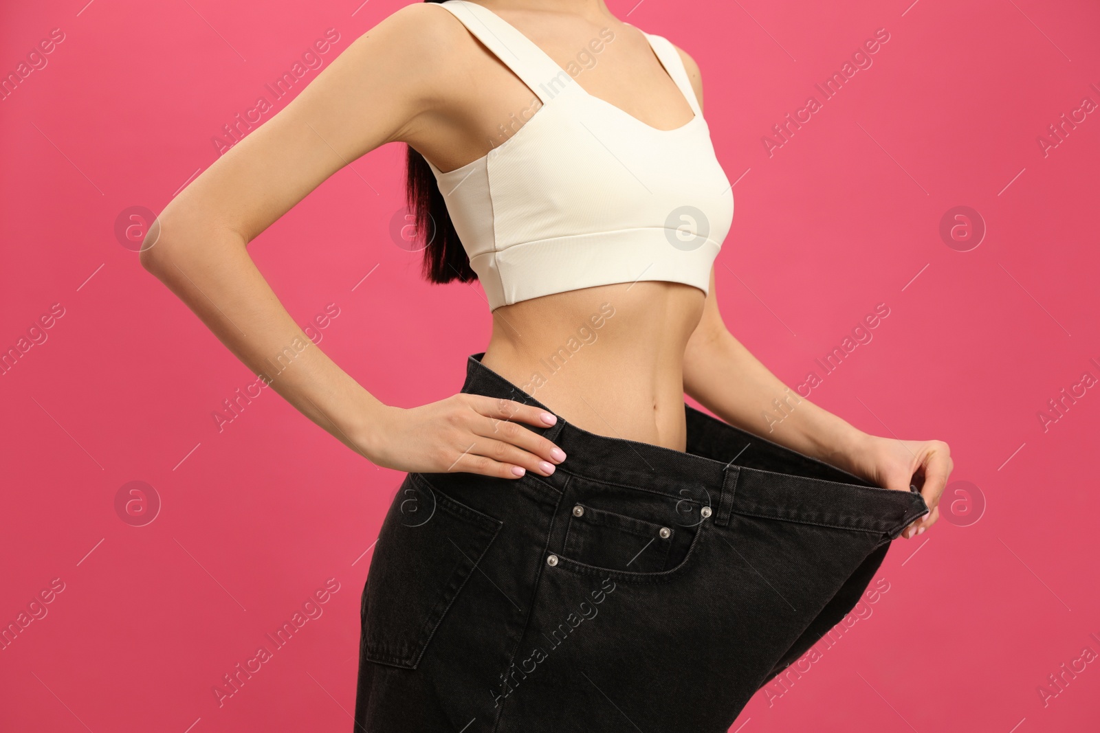 Young woman wearing big jeans after weight loss on pink background, closeup Photo of Young woman wearing big jeans after weight loss on pink background, closeup