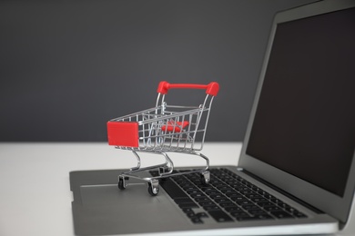 Internet shopping. Laptop with small cart on table against grey background Photo of Internet shopping. Laptop with small cart on table against grey background