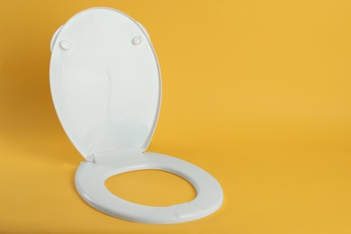 New white plastic toilet seat on yellow background, space for text Photo of New white plastic toilet seat on yellow background, space for text