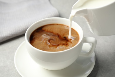 Pouring milk into cup of hot coffee on grey table, closeup Photo of Pouring milk into cup of hot coffee on grey table, closeup