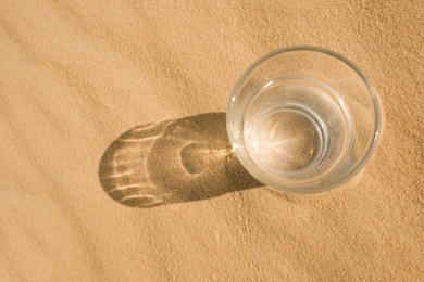 Glass of water on sand in desert, top view. Space for text Photo of Glass of water on sand in desert, top view. Space for text