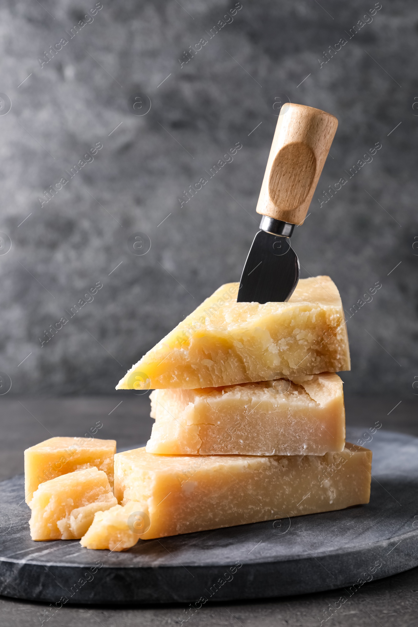 Parmesan cheese with board and knife on grey table Photo of Parmesan cheese with board and knife on grey table