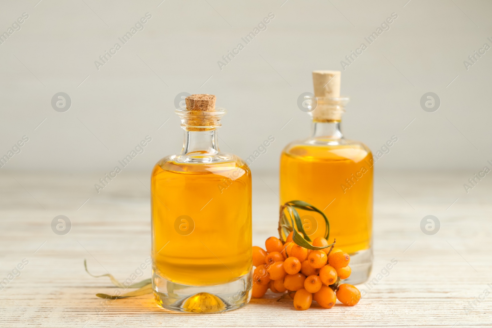 Natural sea buckthorn oil and fresh berries on white wooden table Photo of Natural sea buckthorn oil and fresh berries on white wooden table