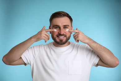 Happy young man applying facial cream on light blue background Photo of Happy young man applying facial cream on light blue background