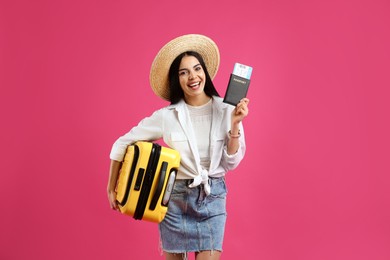 Happy female tourist with suitcase, ticket and passport on pink background Photo of Happy female tourist with suitcase, ticket and passport on pink background