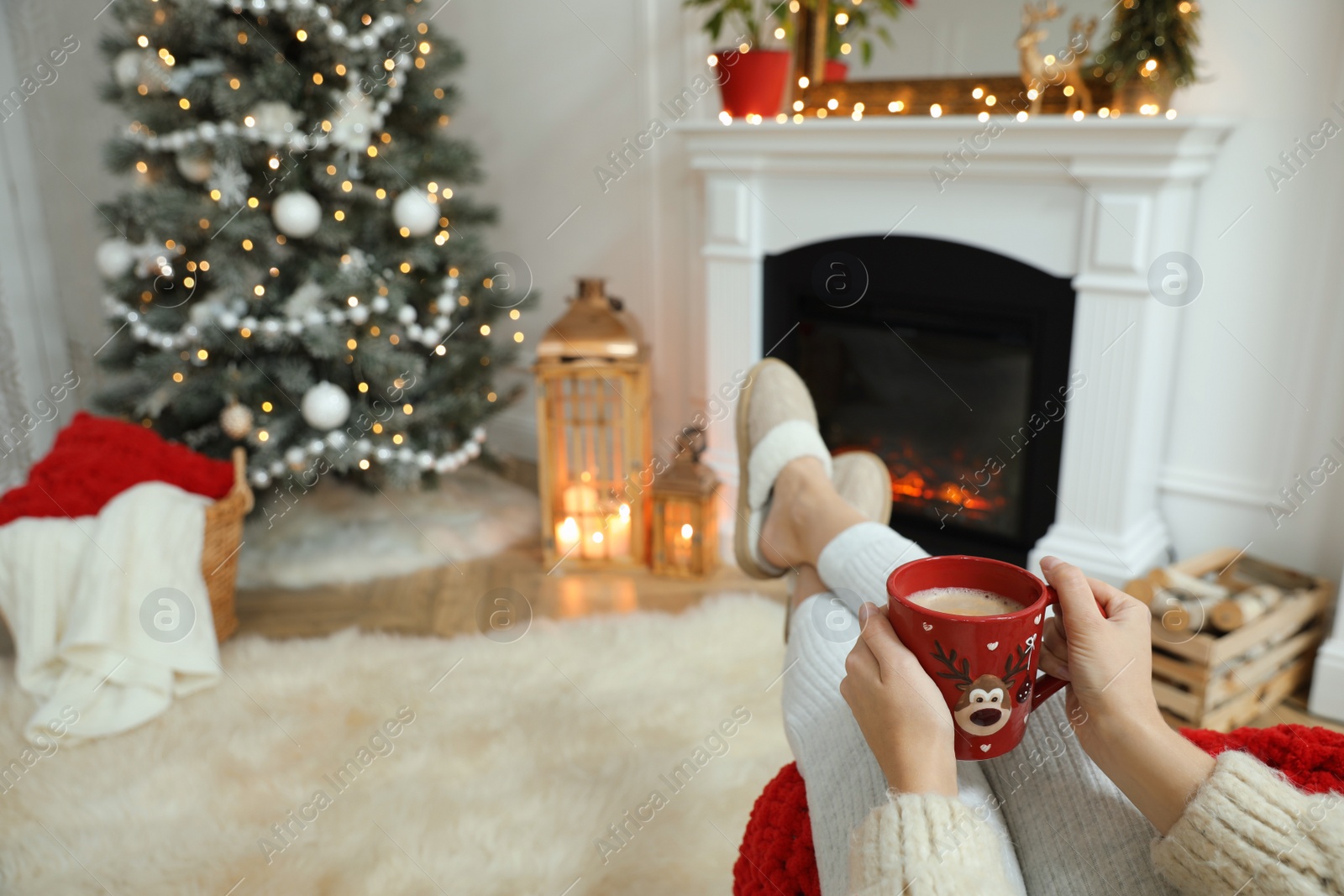 Woman with hot drink resting near fireplace in cozy room decorated for Christmas, closeup Photo of Woman with hot drink resting near fireplace in cozy room decorated for Christmas, closeup