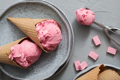 Delicious pink ice cream in wafer cones with candies on grey table, flat lay Photo of Delicious pink ice cream in wafer cones with candies on grey table, flat lay