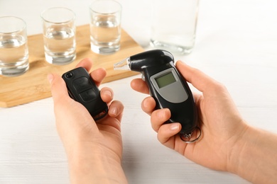 Woman holding modern breathalyzer and car key near white table with alcohol, closeup Photo of Woman holding modern breathalyzer and car key near white table with alcohol, closeup