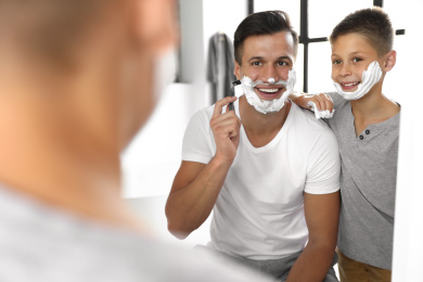 Dad showing his son how to shave near mirror in bathroom Photo of Dad showing his son how to shave near mirror in bathroom