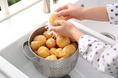 Woman washing fresh potatoes in kitchen sink, closeup Photo of Woman washing fresh potatoes in kitchen sink, closeup
