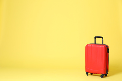 Photo of Stylish red suitcase on yellow background. Space for text