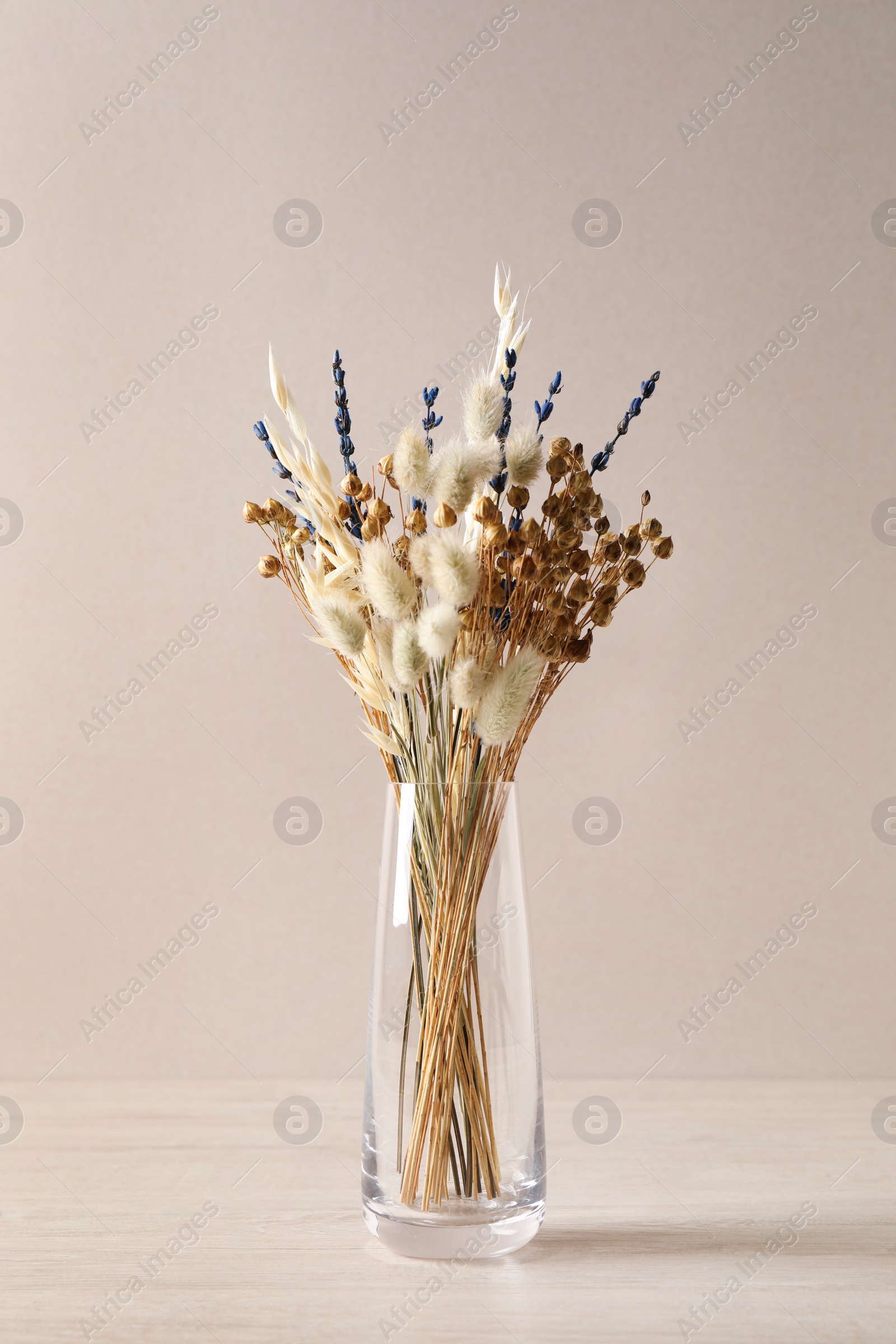 Dried flowers in vase on table against light background Photo of Dried flowers in vase on table against light background