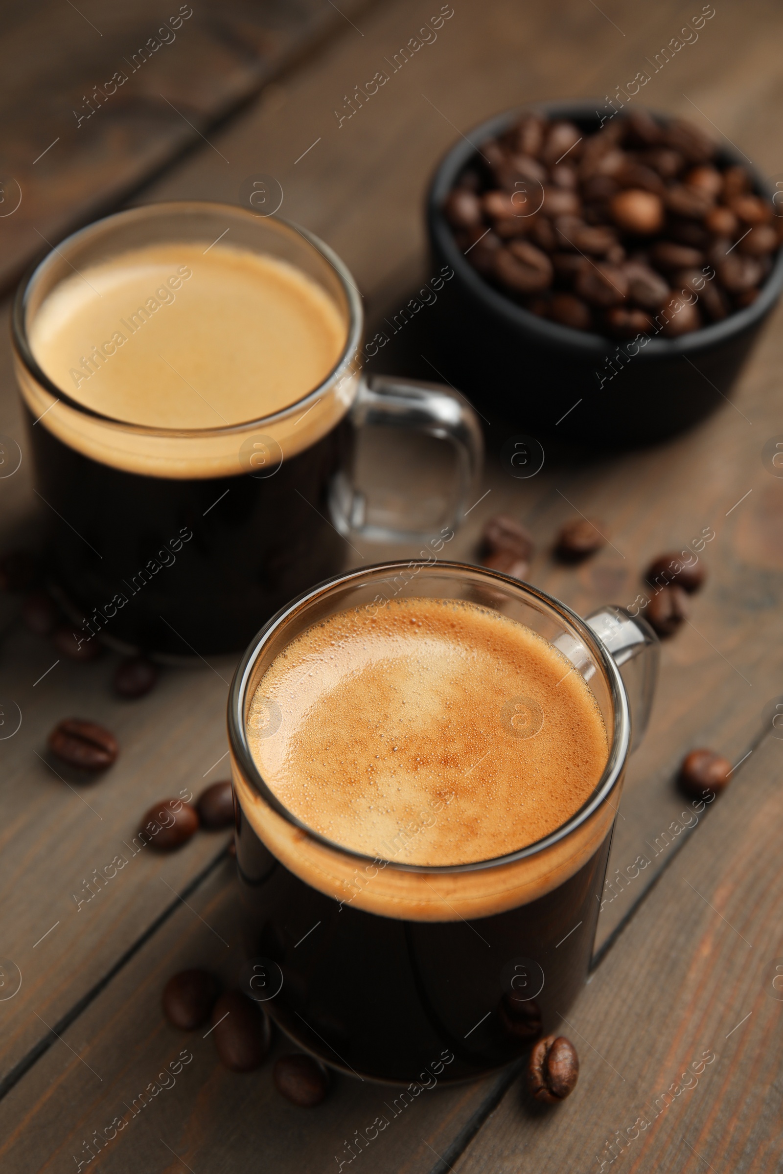 Cups of hot aromatic coffee and roasted beans on wooden table Photo of Cups of hot aromatic coffee and roasted beans on wooden table