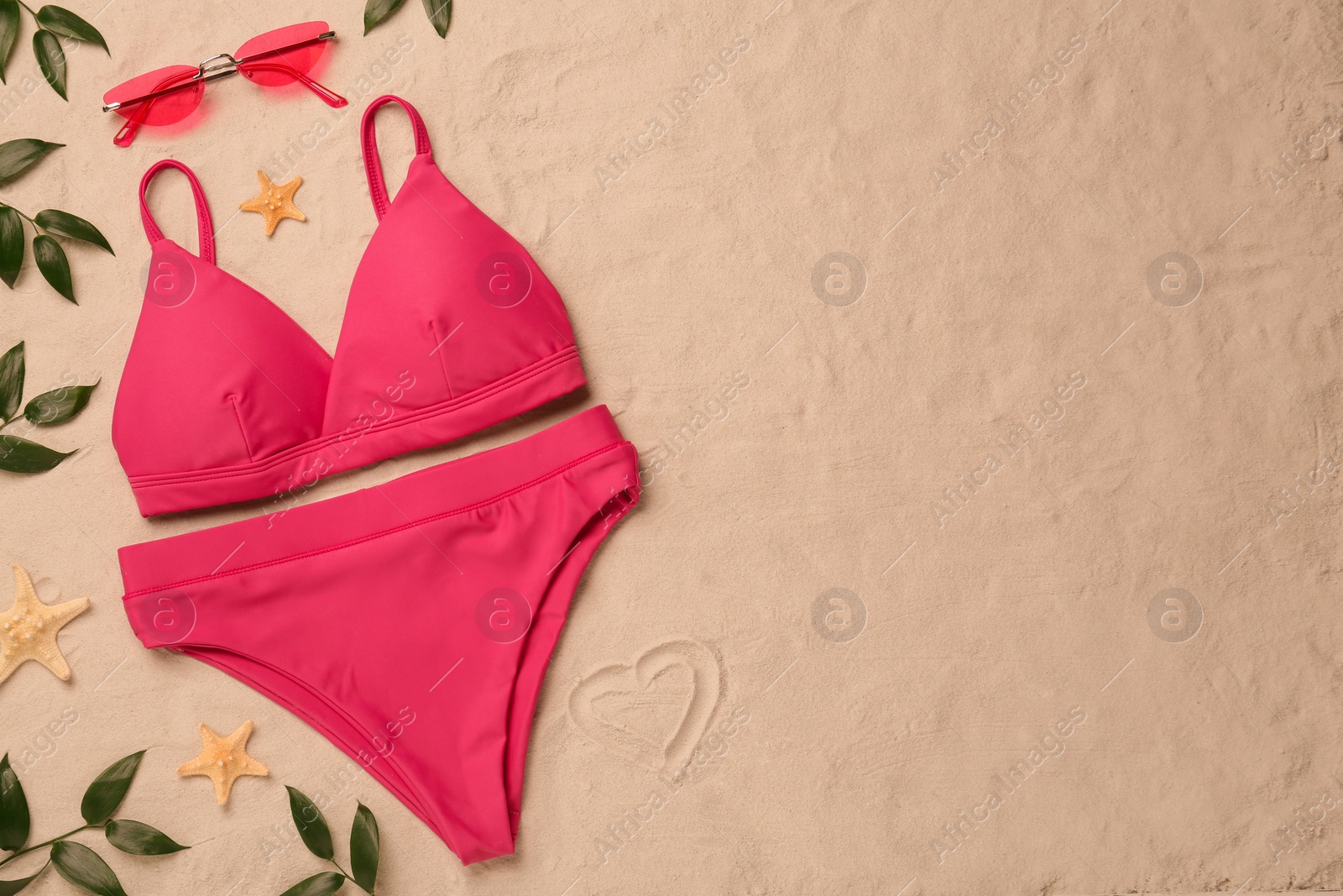 Photo of Stylish bikini and beach accessories on sand, flat lay. Space for text