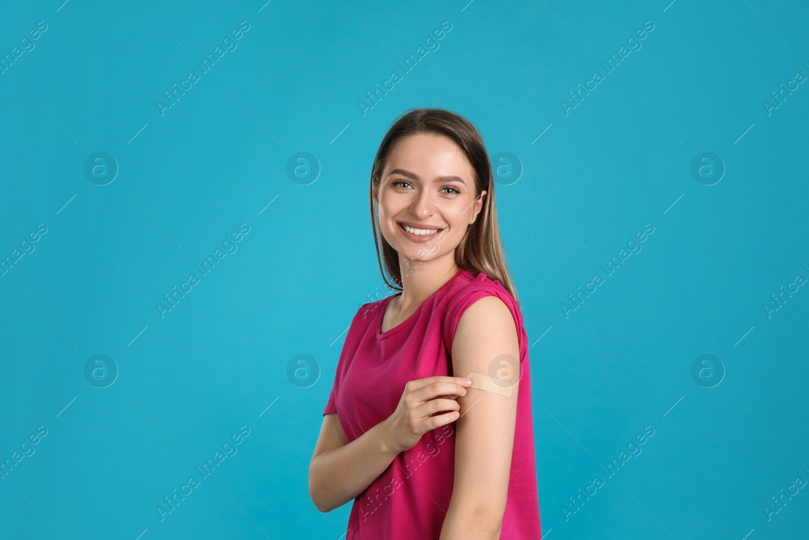 Vaccinated woman showing medical plaster on her arm against light blue background Photo of Vaccinated woman showing medical plaster on her arm against light blue background