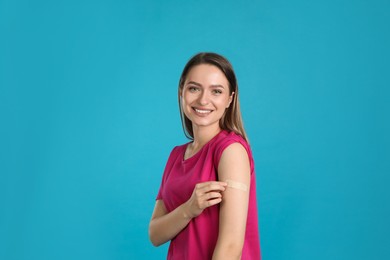 Vaccinated woman showing medical plaster on her arm against light blue background Photo of Vaccinated woman showing medical plaster on her arm against light blue background