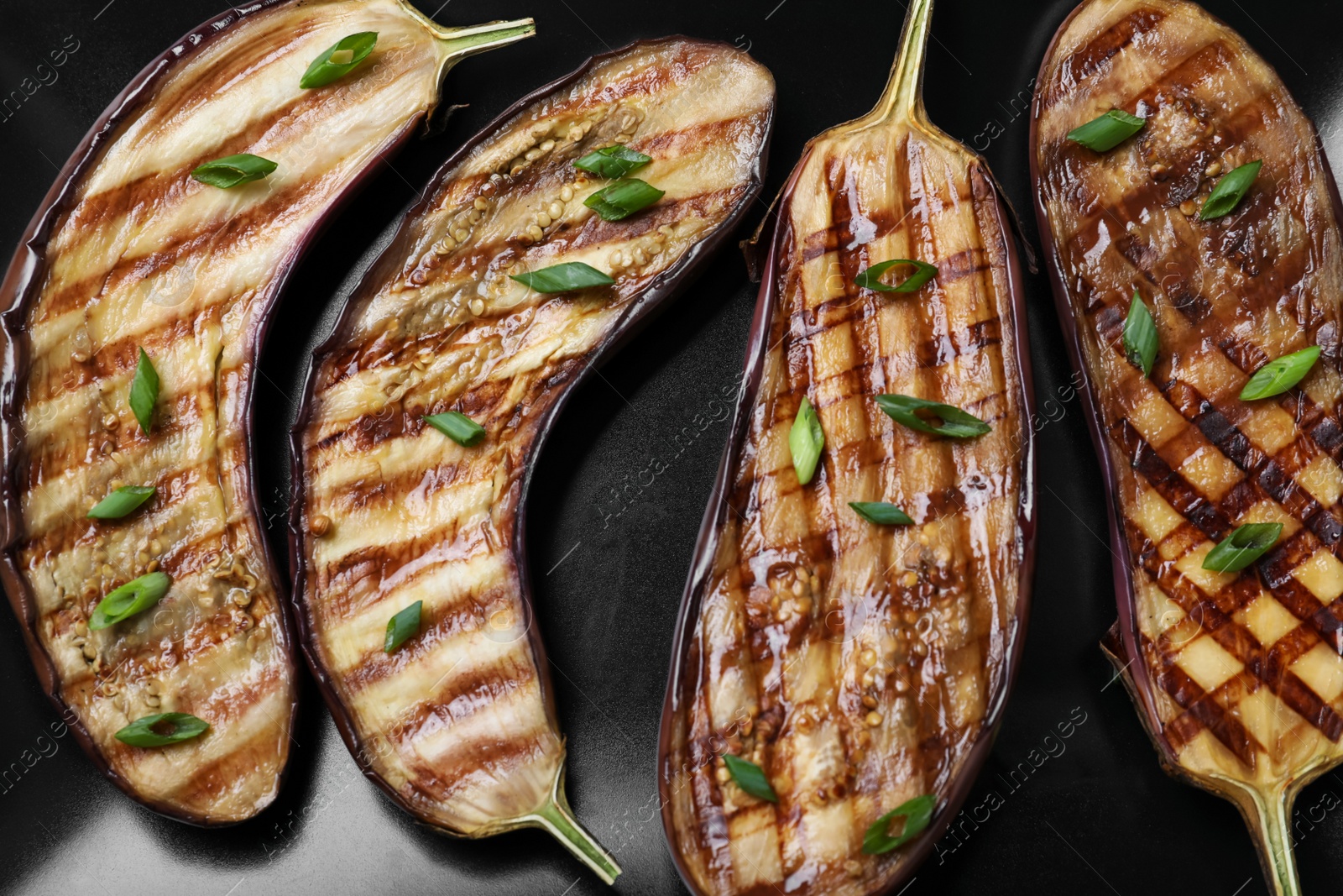 Delicious grilled eggplant halves with green onion on black plate, closeup Photo of Delicious grilled eggplant halves with green onion on black plate, closeup