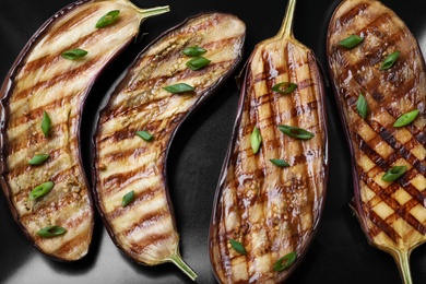 Delicious grilled eggplant halves with green onion on black plate, closeup Photo of Delicious grilled eggplant halves with green onion on black plate, closeup