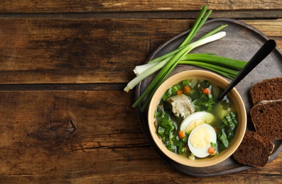 Photo of Delicious sorrel soup with meat and eggs served on wooden table, flat lay. Space for text