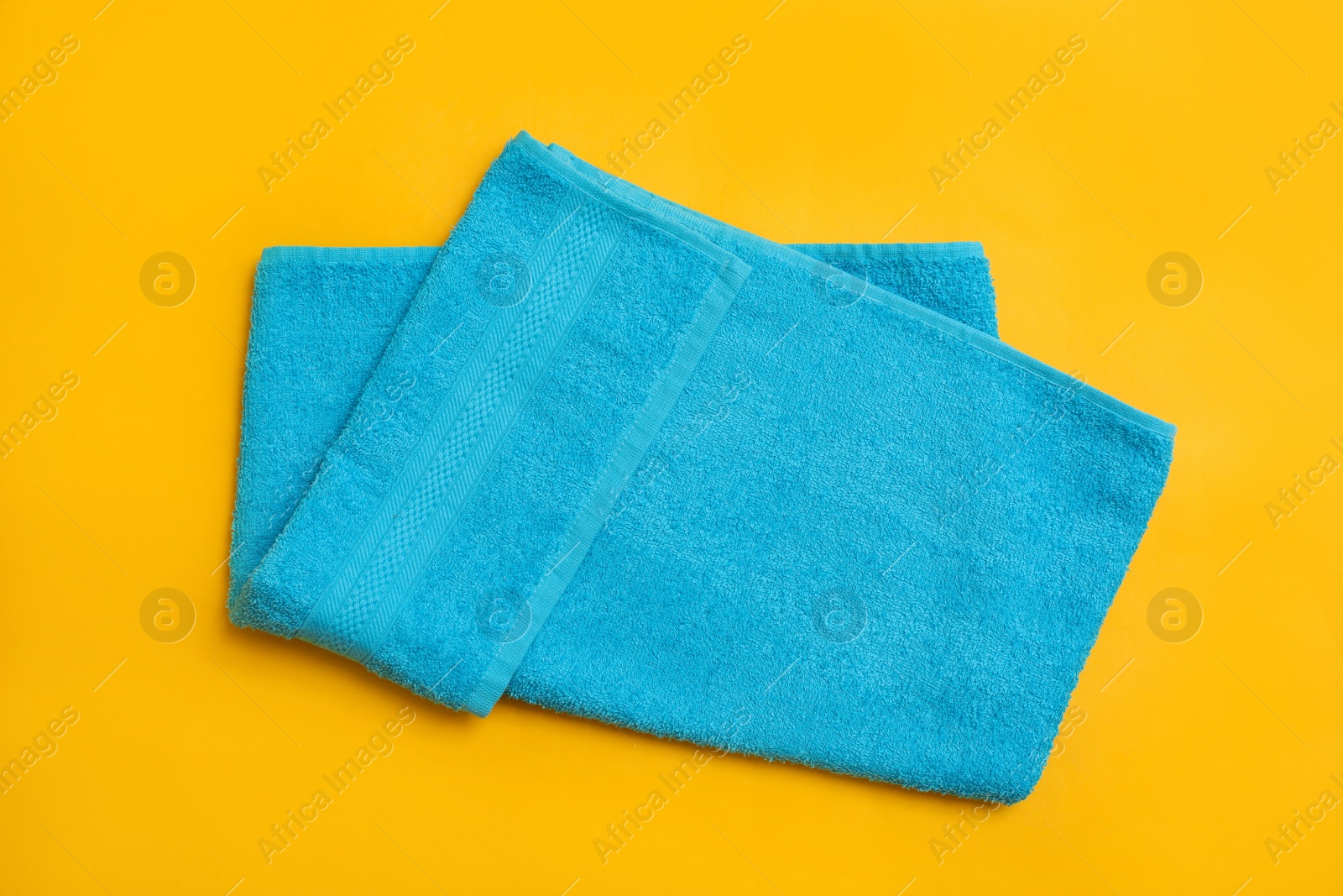 Folded light blue beach towel on yellow background, top view Photo of Folded light blue beach towel on yellow background, top view