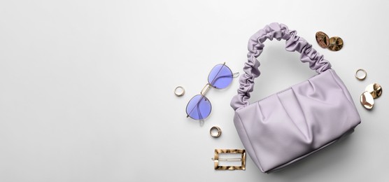 Photo of Stylish woman's bag, sunglasses and bijouterie on light background, flat lay