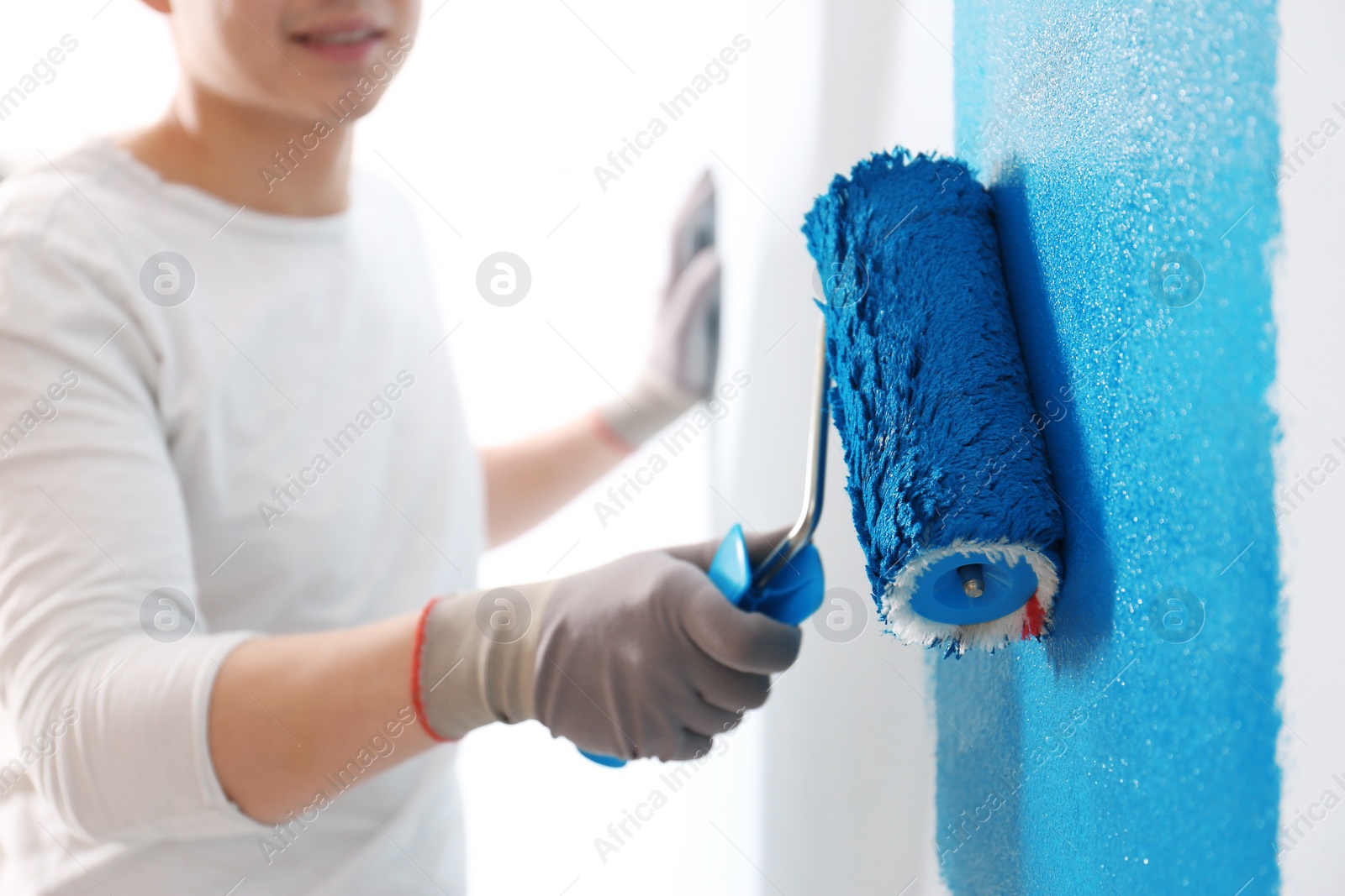 Male decorator painting wall with roller indoors, closeup Photo of Male decorator painting wall with roller indoors, closeup